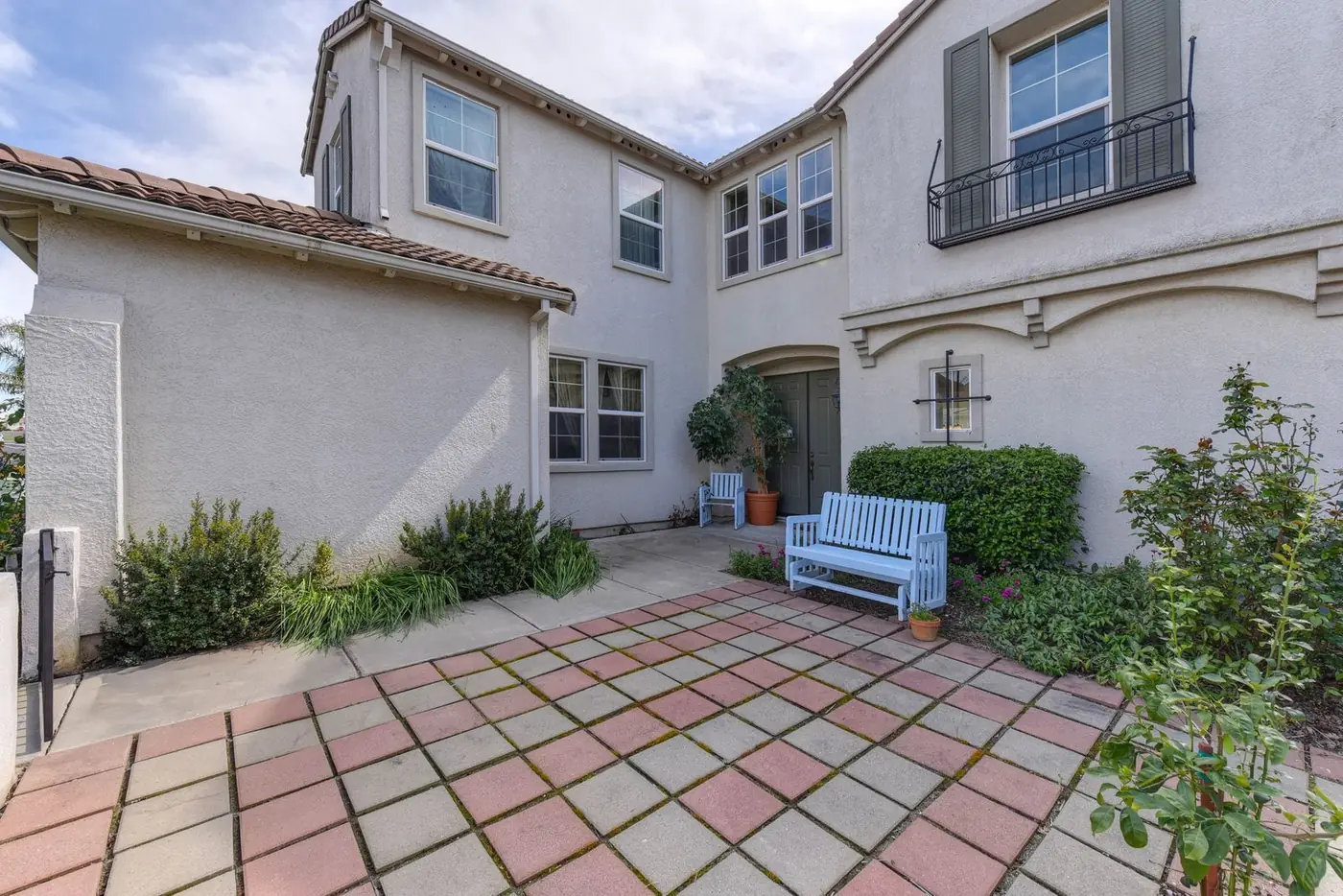 Front entry court of a cream stucco home, paved in red and gray square pavers