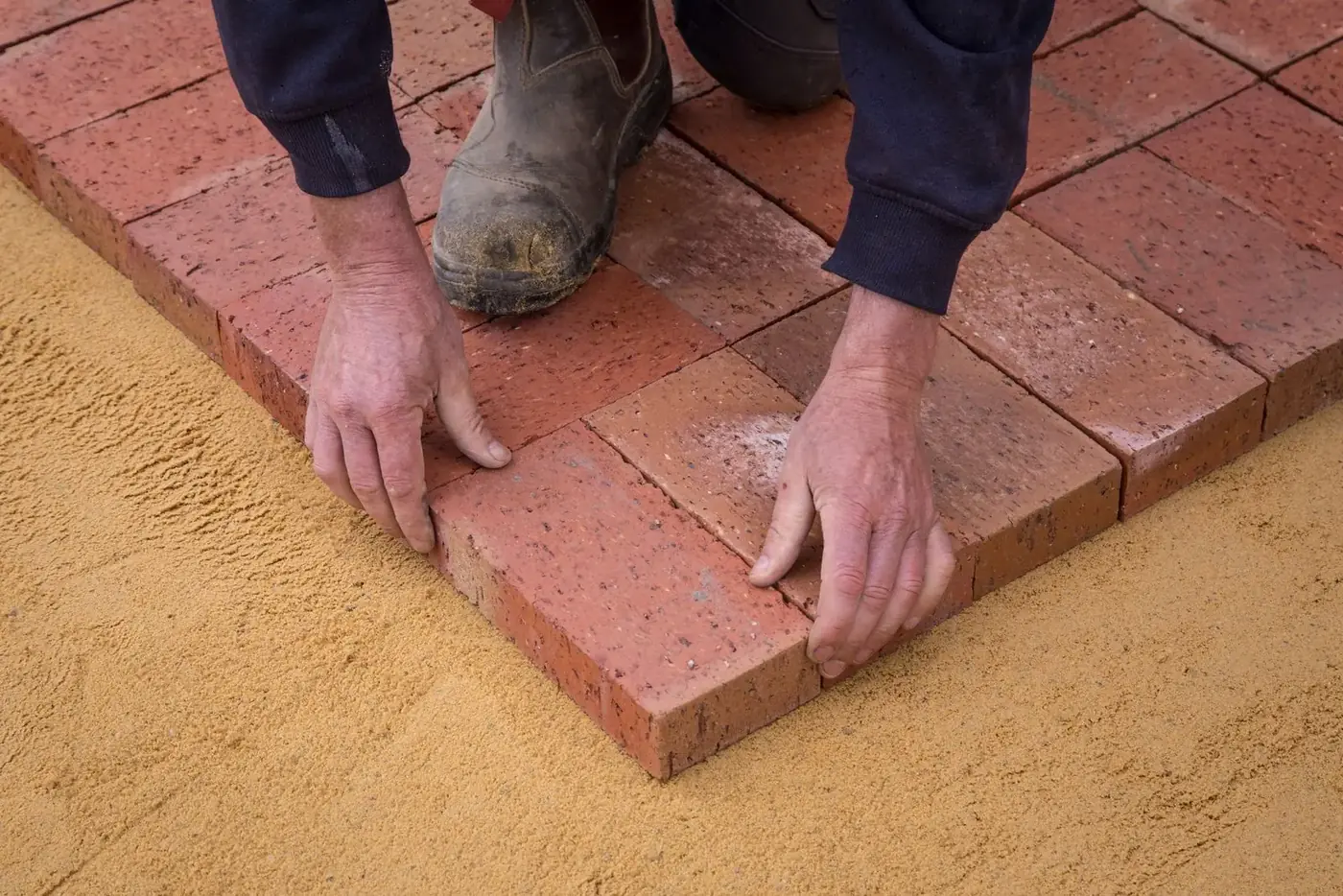Hands setting brick pavers on a screeded sand bed