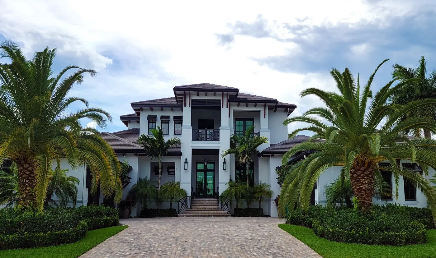 Concrete paver driveway leading to a white stucco home with palms