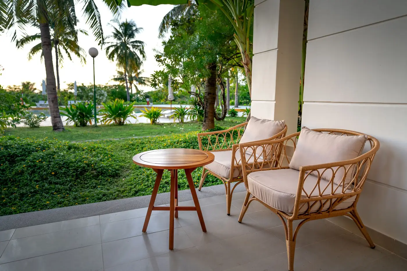 Covered tile patio with rattan armchairs overlooking a lawn and palm trees